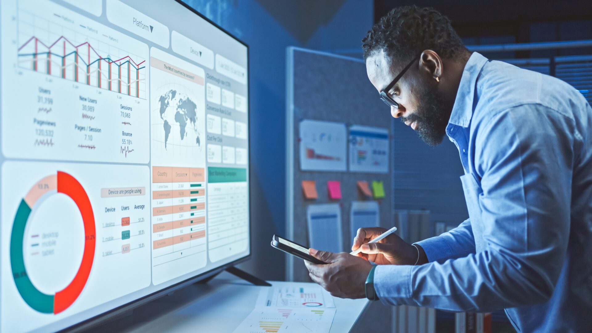 A man analyzes data on a large screen and tablet in a modern office.